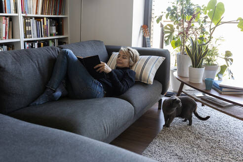 Mature woman relaxing on couch at home reading a book - VABF02376