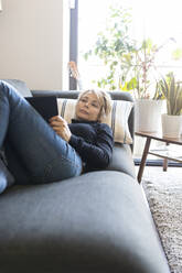 Mature woman relaxing on couch at home reading a book - VABF02377