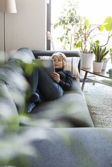 Reife Frau entspannt sich auf der Couch zu Hause mit Tablet - VABF02378
