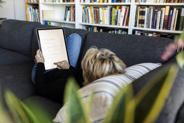 Reife Frau entspannt sich zu Hause auf der Couch mit einem Grafiktablett - VABF02380