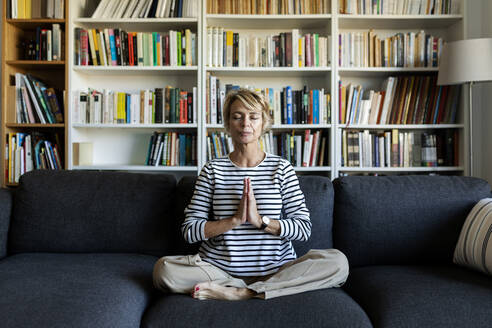 Reife Frau übt Yoga auf der Couch zu Hause - VABF02406