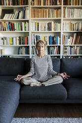 Mature woman practicing yoga on couch at home - VABF02407
