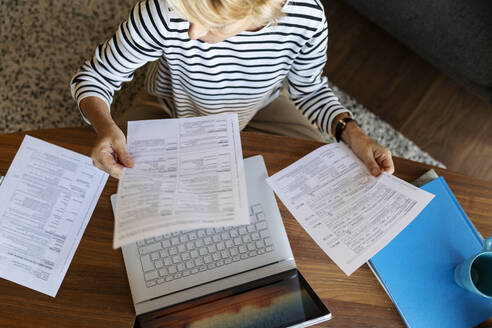 Mature woman with documents using laptop at home - VABF02411