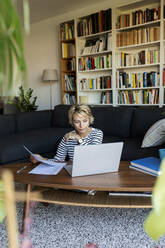 Reife Frau mit Dokumenten am Laptop zu Hause - VABF02413