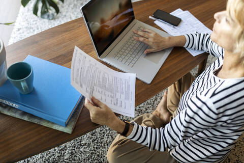 Reife Frau mit Dokumenten am Laptop zu Hause, lizenzfreies Stockfoto