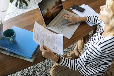 Reife Frau mit Dokumenten am Laptop zu Hause - VABF02414