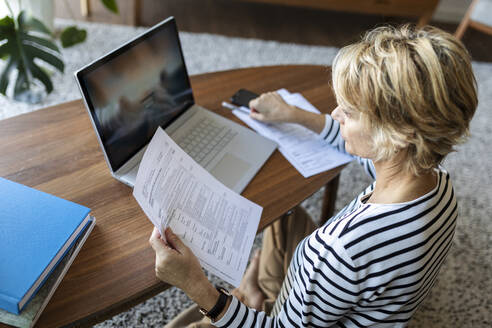 Reife Frau mit Dokumenten am Laptop zu Hause - VABF02415