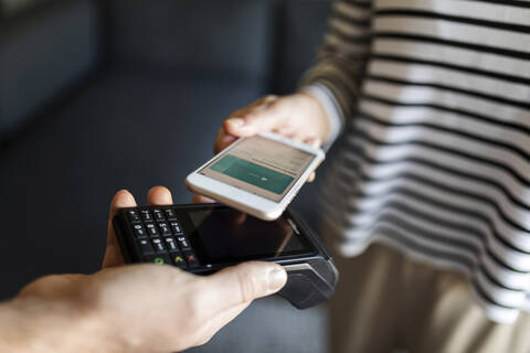 Nahaufnahme einer Frau, die zu Hause mit ihrem Mobiltelefon bezahlt, lizenzfreies Stockfoto