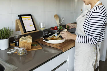 Nahaufnahme einer Frau mit Tablet beim Kochen eines Nudelgerichts in der Küche zu Hause - VABF02446