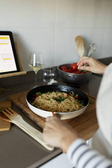 Close-up of woman with tablet cooking pasta dish in kitchen at home - VABF02447