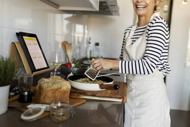 Glückliche reife Frau mit Tablet Kochen Pasta Gericht in der Küche zu Hause - VABF02448