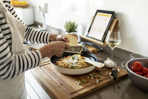 Nahaufnahme einer Frau mit Tablet beim Kochen eines Nudelgerichts in der Küche zu Hause - VABF02451