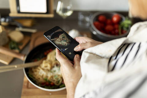 Nahaufnahme einer Frau, die ein Smartphone-Foto von ihrem Nudelgericht in der Küche zu Hause macht, lizenzfreies Stockfoto