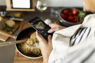 Nahaufnahme einer Frau, die ein Smartphone-Foto von ihrem Nudelgericht in der Küche zu Hause macht - VABF02452