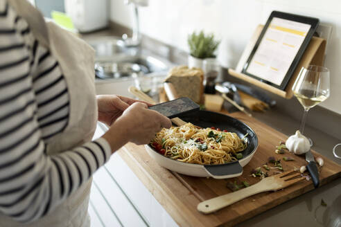 Close-up of woman taking smartphone picture of her pasta dish in kitchen at home - VABF02453