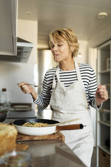 Ältere Frau, die ein hausgemachtes Nudelgericht in der Küche zu Hause probiert - VABF02455