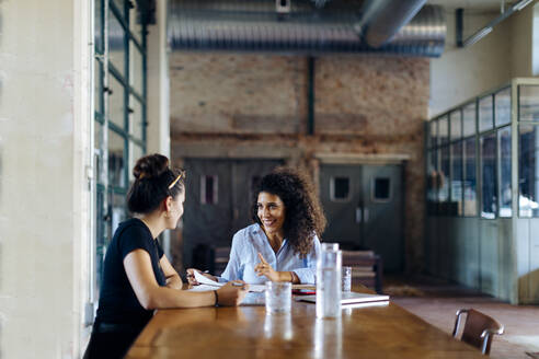Zwei junge Geschäftsfrauen im Gespräch am Konferenztisch im Loftbüro - SODF00353