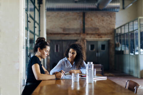 Zwei junge Geschäftsfrauen im Gespräch am Konferenztisch im Loftbüro, lizenzfreies Stockfoto
