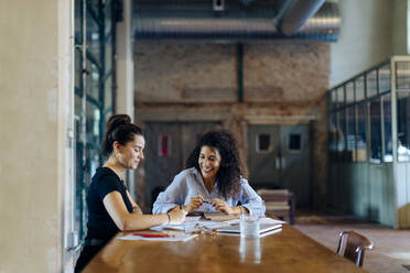 Two young businesswomen talking at conference table in loft office - SODF00355
