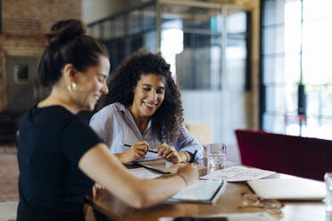 Two young businesswomen working together at conference table in loft office - SODF00356