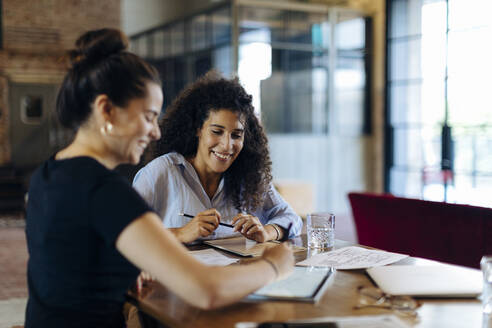 Zwei junge Geschäftsfrauen arbeiten zusammen an einem Konferenztisch in einem Loftbüro - SODF00356