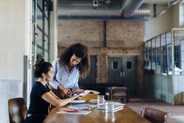 Two young businesswomen talking at conference table in loft office - SODF00357