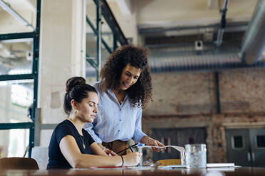 Two young businesswomen talking at conference table in loft office - SODF00358