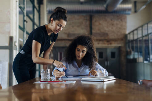 Two young businesswomen talking at conference table in loft office - SODF00359