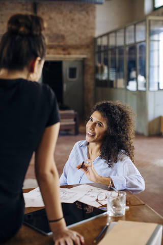 Zwei junge Geschäftsfrauen unterhalten sich am Tisch im Loftbüro, lizenzfreies Stockfoto