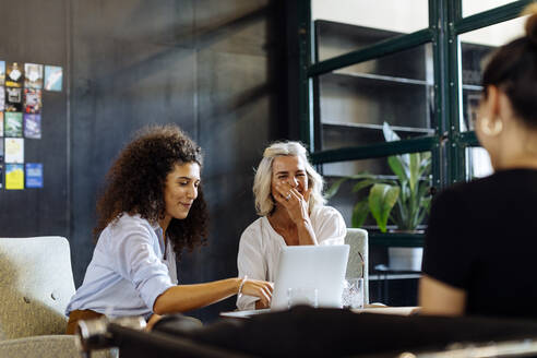 Glückliche Geschäftsfrauen mit Laptop arbeiten zusammen in einem Loft-Büro - SODF00369