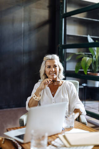 Porträt einer lächelnden reifen Geschäftsfrau mit Laptop in einem Loftbüro, lizenzfreies Stockfoto