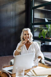 Portrait of smiling mature businesswoman with laptop in loft office - SODF00371