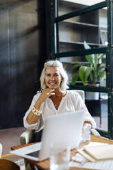 Portrait of smiling mature businesswoman with laptop in loft office - SODF00372