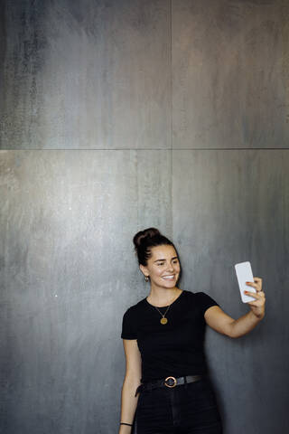 Porträt einer fröhlichen, lässigen jungen Geschäftsfrau, die ein Smartphone vor einer grauen Wand benutzt, lizenzfreies Stockfoto