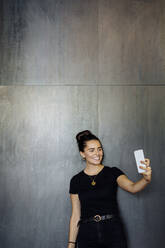 Porträt einer fröhlichen, lässigen jungen Geschäftsfrau, die ein Smartphone vor einer grauen Wand benutzt - SODF00380