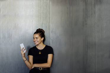Porträt einer fröhlichen, lässigen jungen Geschäftsfrau, die ein Smartphone vor einer grauen Wand benutzt - SODF00383