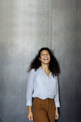 Porträt einer lachenden jungen Geschäftsfrau, die vor einer grauen Wand steht - SODF00387
