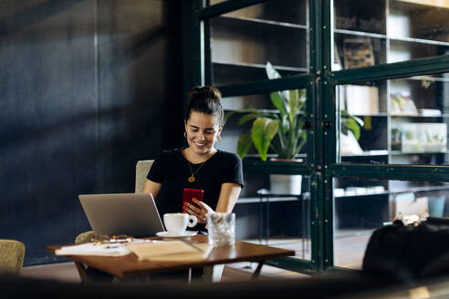 Lässige junge Geschäftsfrau mit Laptop und Smartphone im Loftbüro - SODF00391