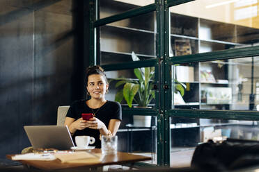 Casual young businesswoman with laptop and smartphone in loft office - SODF00393