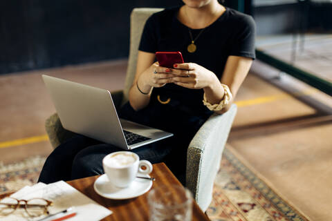 Nahaufnahme einer jungen Geschäftsfrau mit Laptop und Smartphone in einem Loftbüro, lizenzfreies Stockfoto