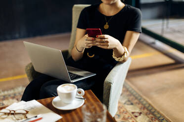 Close-up of young businesswoman with laptop and smartphone in loft office - SODF00394