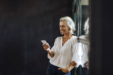 Smiling casual mature businesswoman using smartphone at the window in loft office stock photo