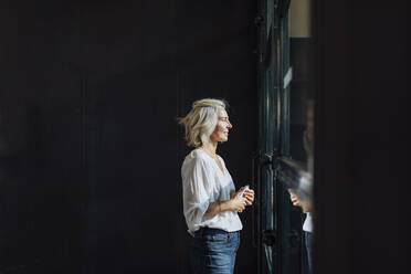 Casual mature businesswoman looking out of window in loft office - SODF00396