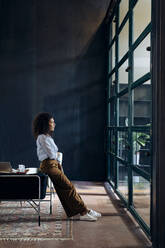 Junge Geschäftsfrau schaut aus dem Fenster in einem Loftbüro - SODF00406