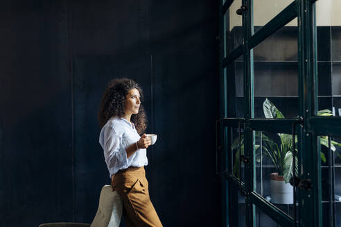 Young businesswoman looking out of window in loft office - SODF00408