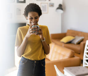 Happy young woman holding mug at home - GIOF07779