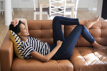 Relaxed young woman lying on couch at home - GIOF07780