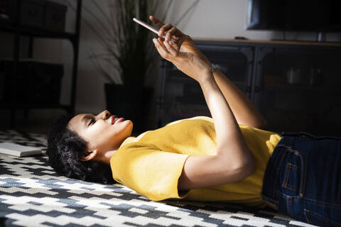 Junge Frau liegt zu Hause auf dem Boden und benutzt ihr Smartphone, lizenzfreies Stockfoto