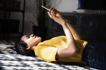 Young woman lying on the floor at home using smartphone - GIOF07785