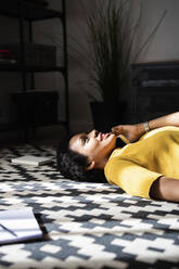 Young woman lying on the floor at home talking on the phone - GIOF07786